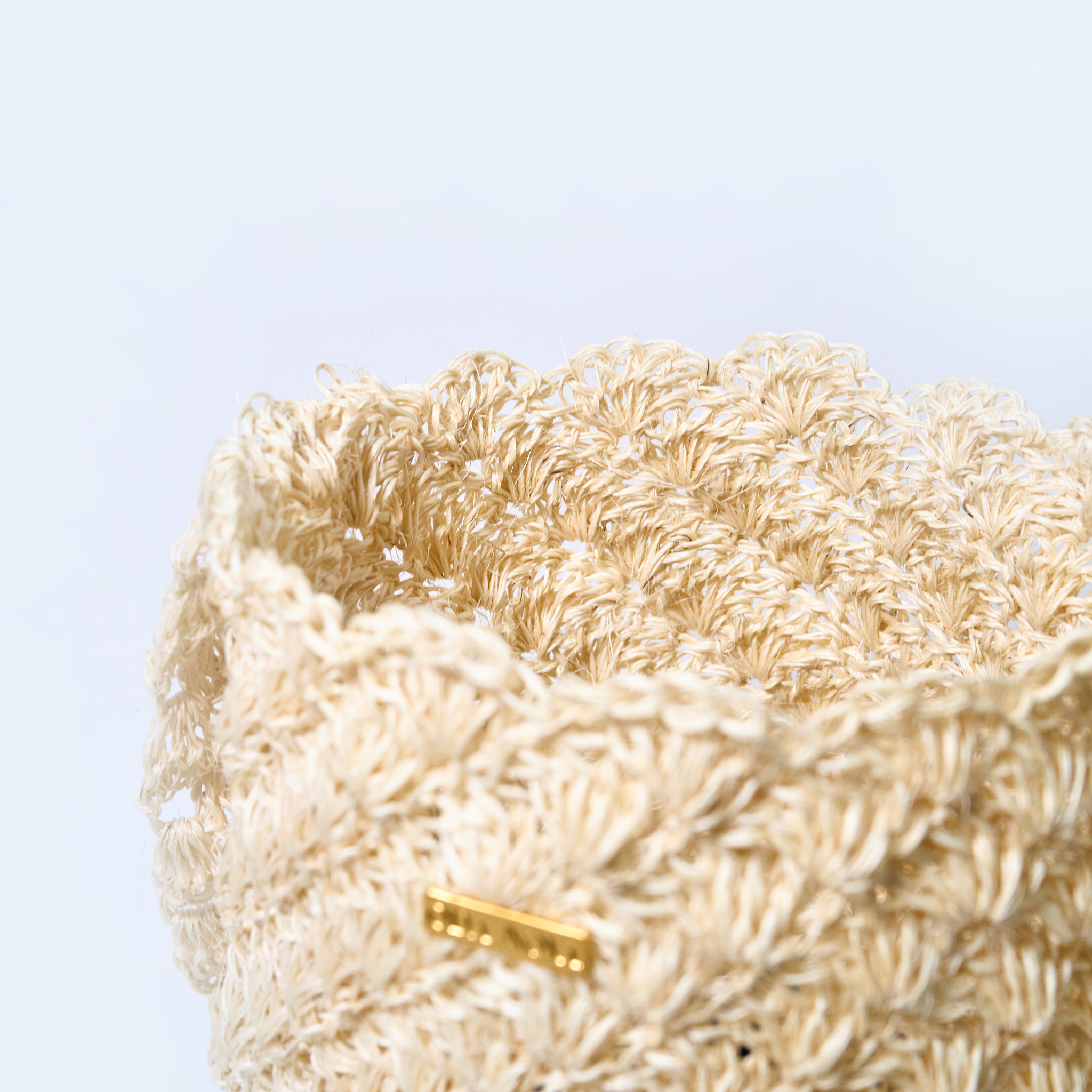 Close-up solstice handcrafted crossbody bag made from natural fique fiber in beige, designed by Oda Nova with ancestral Colombian techniques
Closeup with a gold tag on a light blue background
